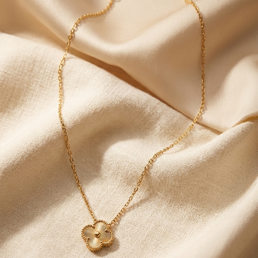 Gold necklace with a clover-shaped pendant on beige fabric