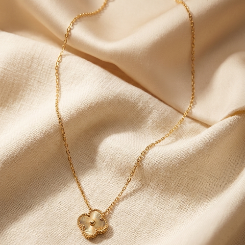 Gold necklace with a clover-shaped pendant on beige fabric