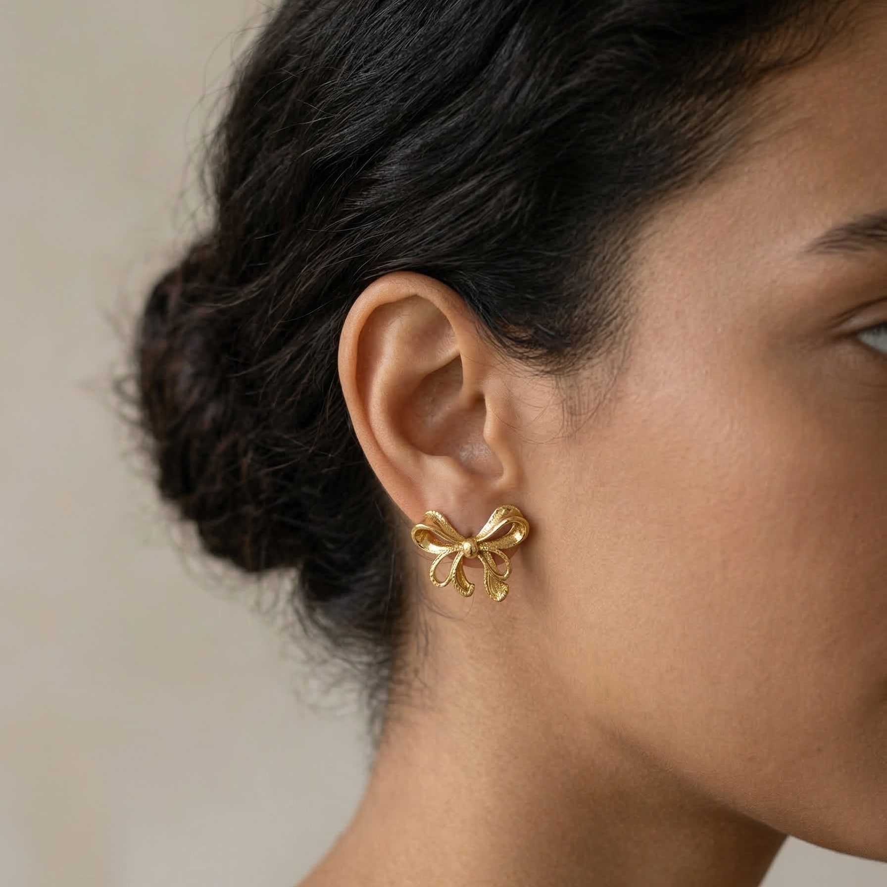 Close-up of a person wearing a gold earring with a neutral background