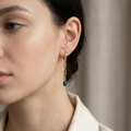 Close-up of a person wearing gold earrings with a dark stone against a neutral background