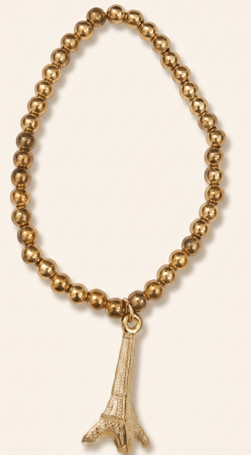 Gold beaded bracelet with Eiffel Tower charm on a beige background