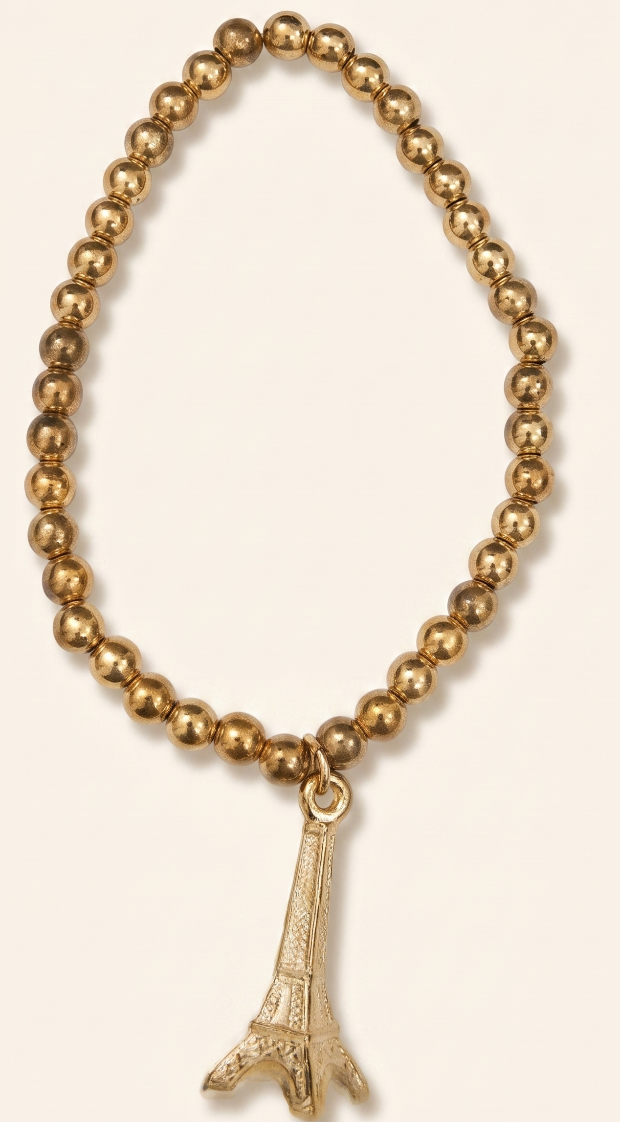 Gold beaded bracelet with Eiffel Tower charm on a beige background