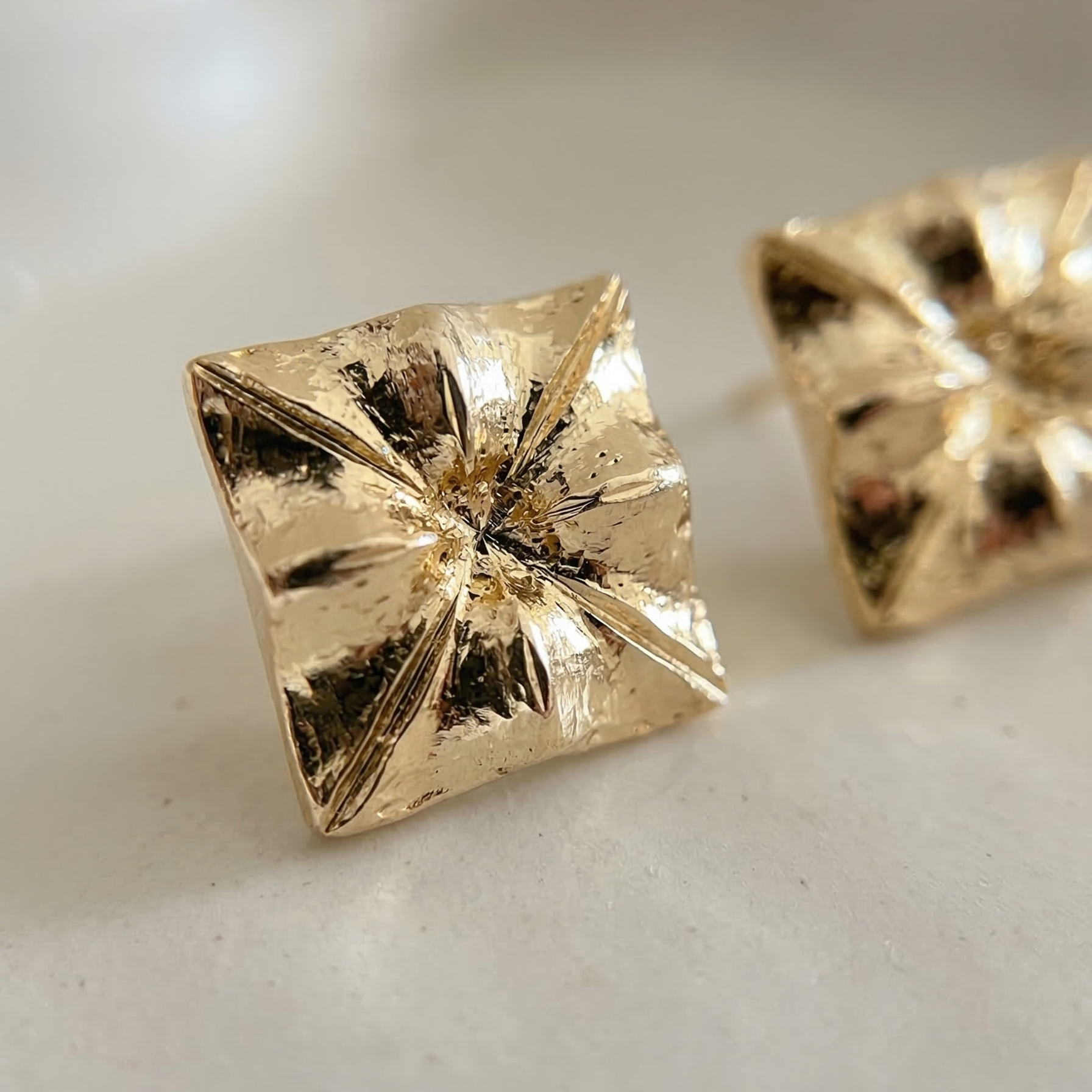 Gold pyramid-shaped earrings on a light background