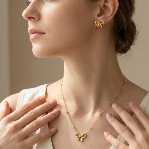Woman wearing a gold bow necklace and earrings against a neutral background