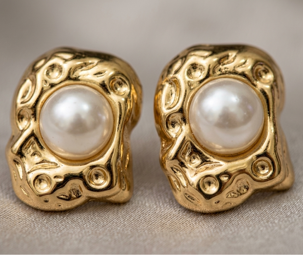 Pair of gold earrings with pearl centers on a neutral background