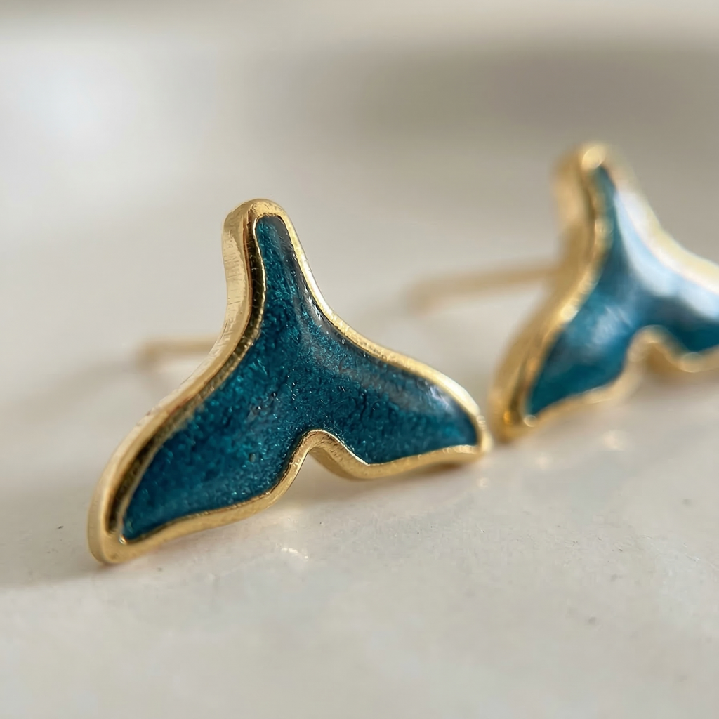 Blue whale tail earrings with gold accents on a white background