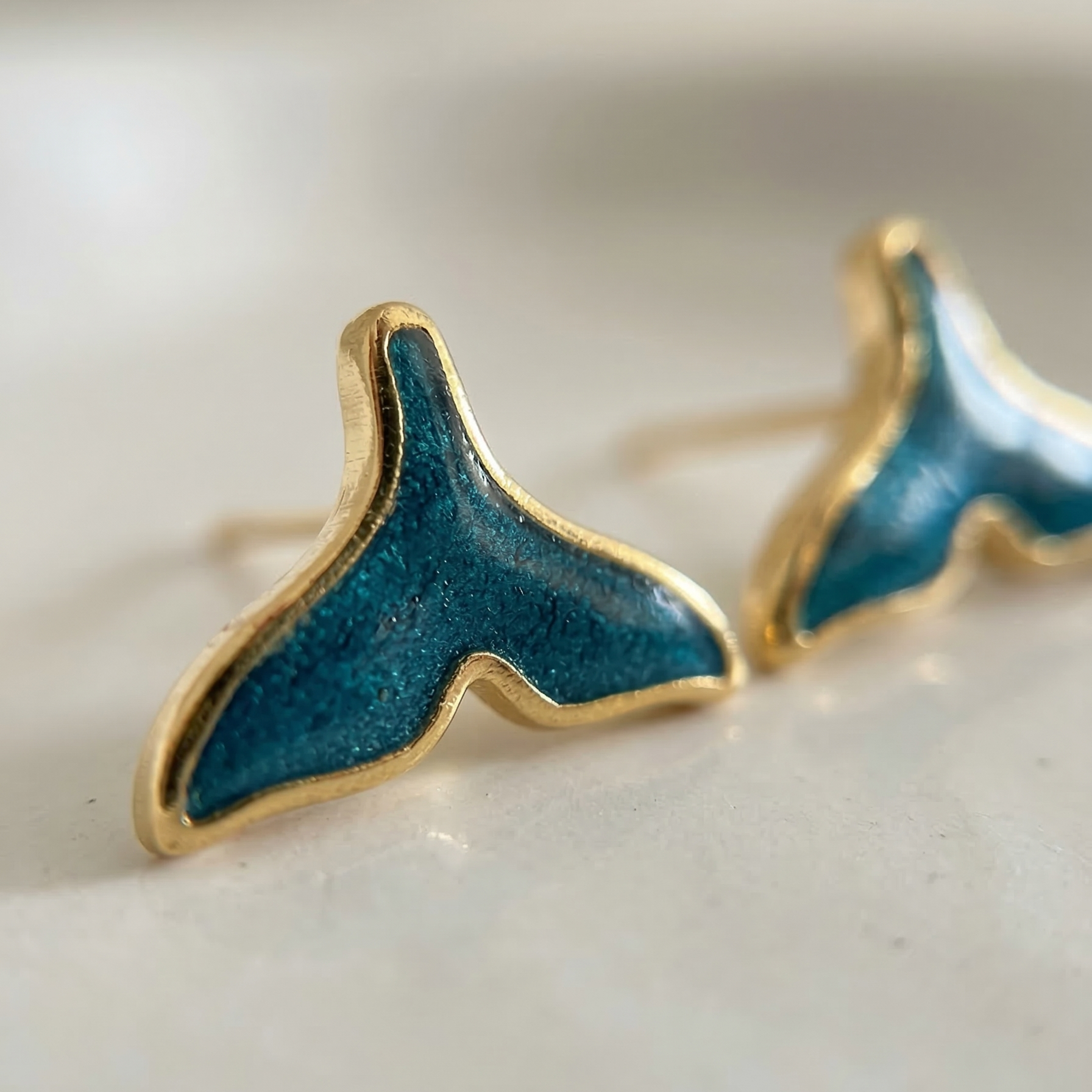 Blue whale tail earrings with gold accents on a white background