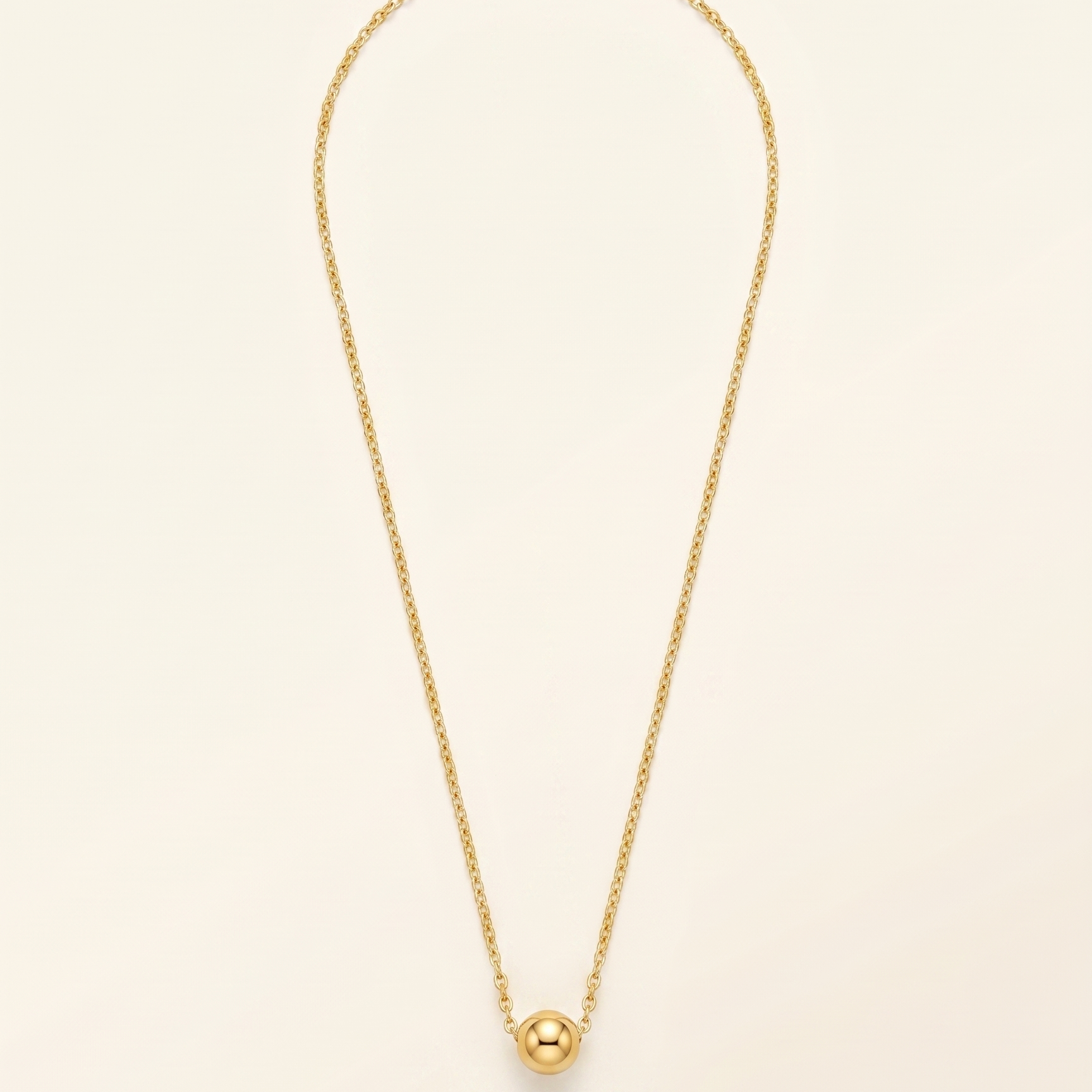 Gold necklace with a single pearl pendant on a beige background