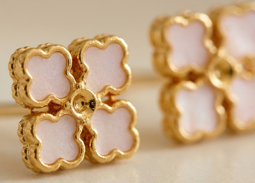 Gold and pink flower-shaped earrings on a beige background