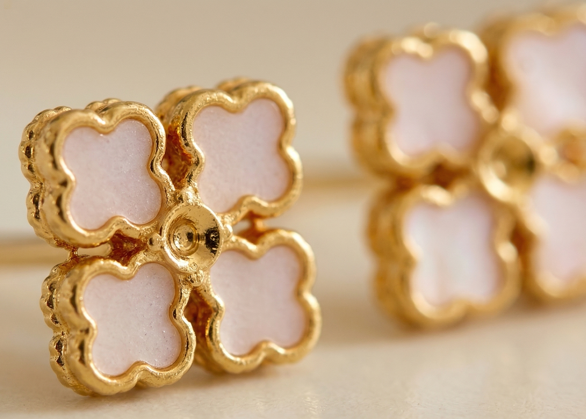 Gold and pink flower-shaped earrings on a beige background