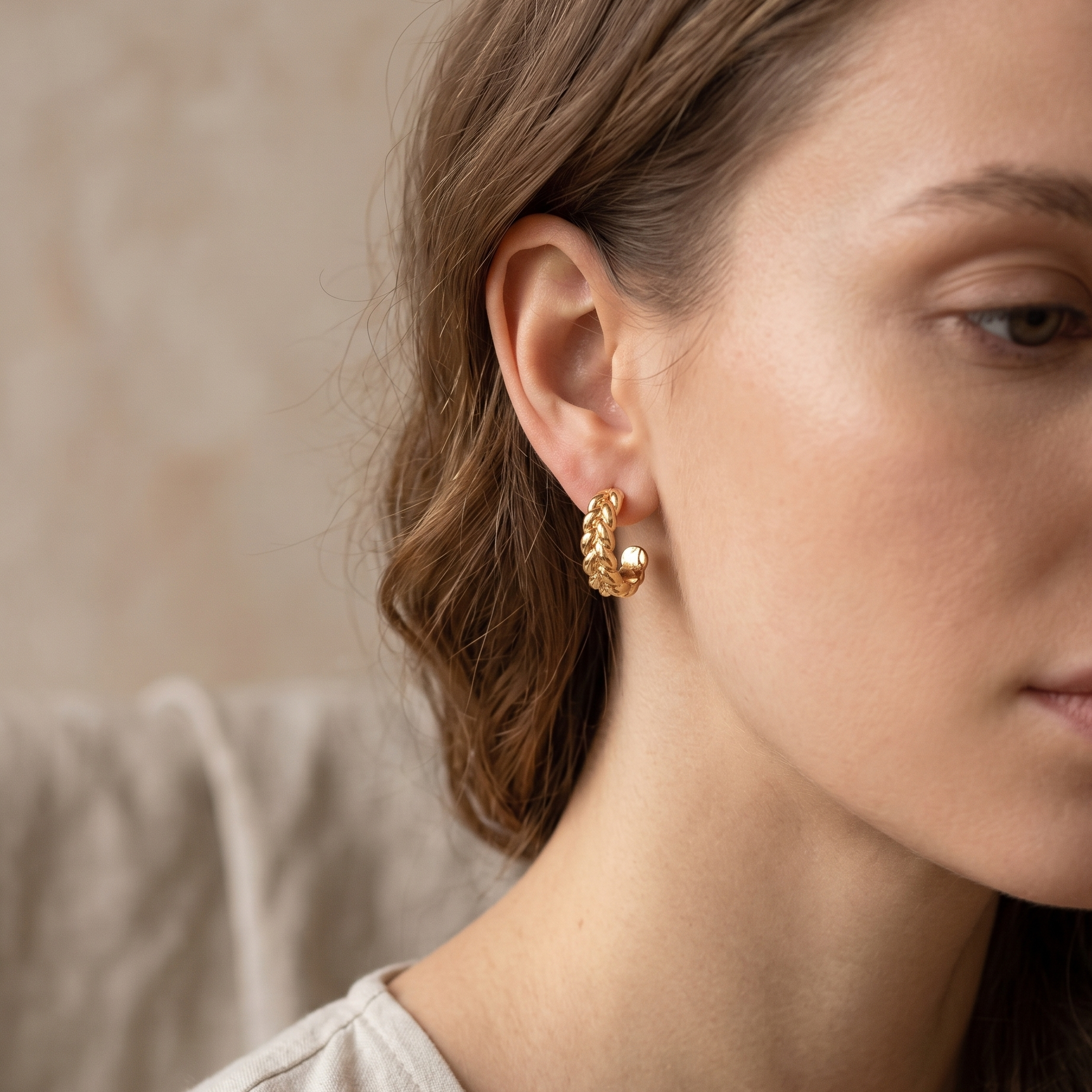 Close-up of a woman wearing gold earrings with a neutral background