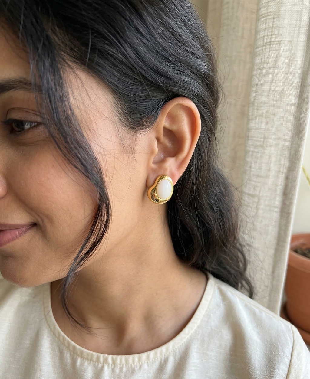 Woman wearing a gold earring with a pearl-like center, smiling softly.