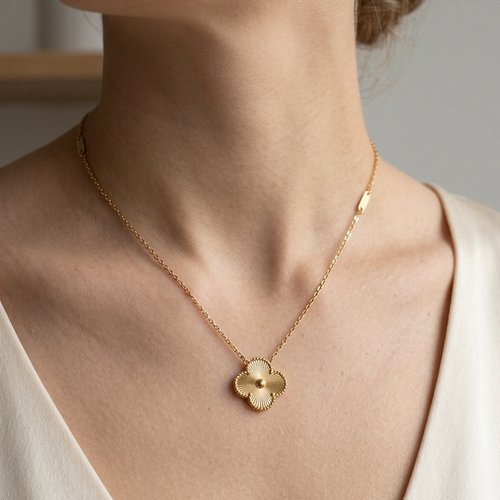 Gold necklace with a clover-shaped pendant worn by a person in a white top.