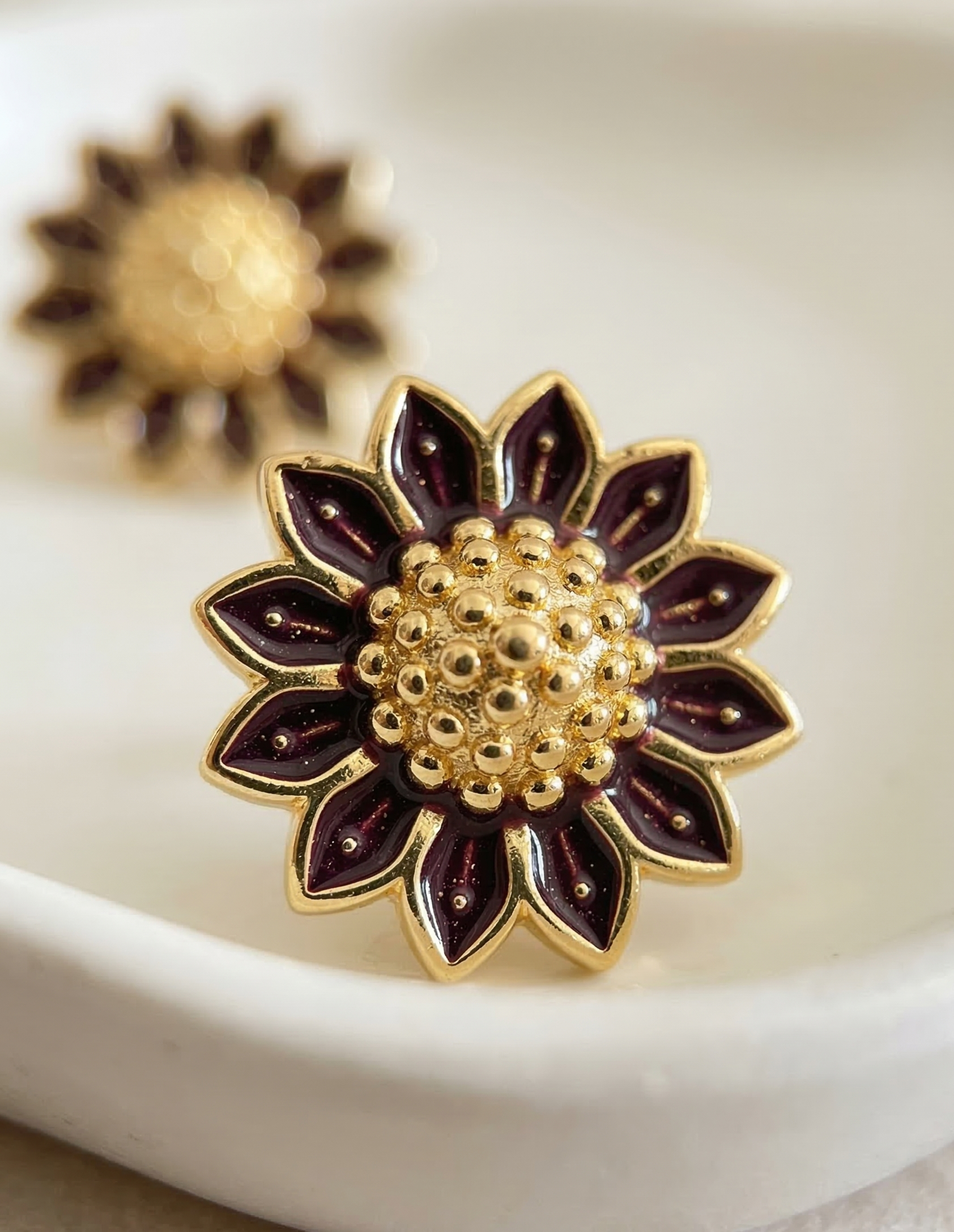 Gold and purple sunflower-shaped earrings on a white dish.
