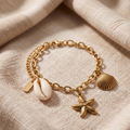 Gold bracelet with shell and starfish charms on a beige fabric background