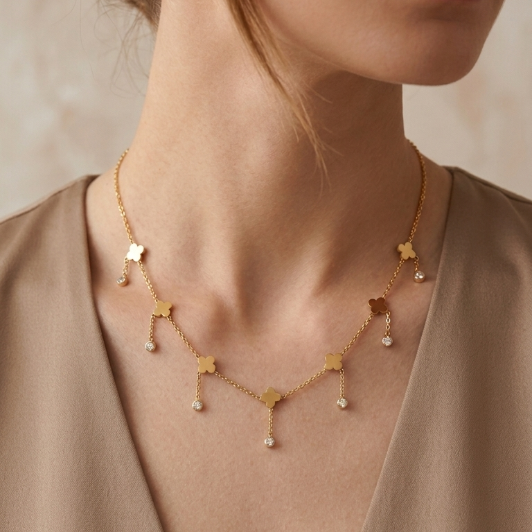 A close-up of a woman wearing a delicate gold necklace with small star-shaped charms and tiny clear crystal drops, styled with a taupe top.