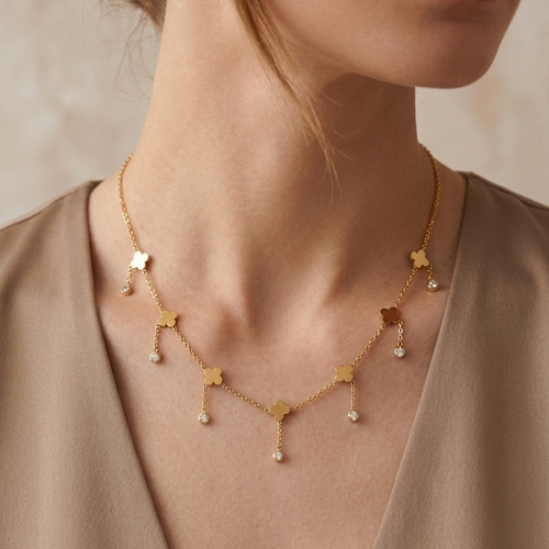 A close-up of a woman wearing a delicate gold necklace with small star-shaped charms and tiny clear crystal drops, styled with a taupe top.