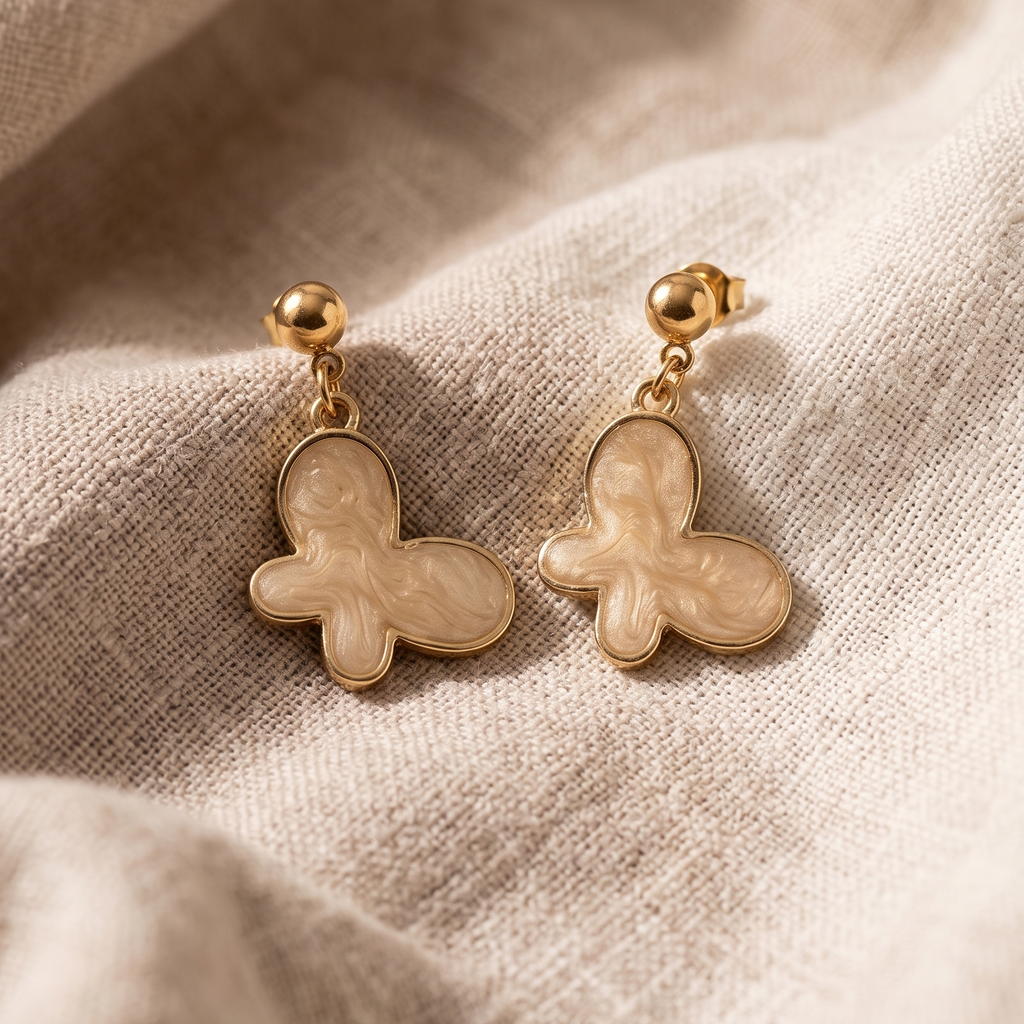 Pair of gold butterfly earrings on a beige fabric background