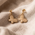 Pair of gold butterfly earrings on a beige fabric background