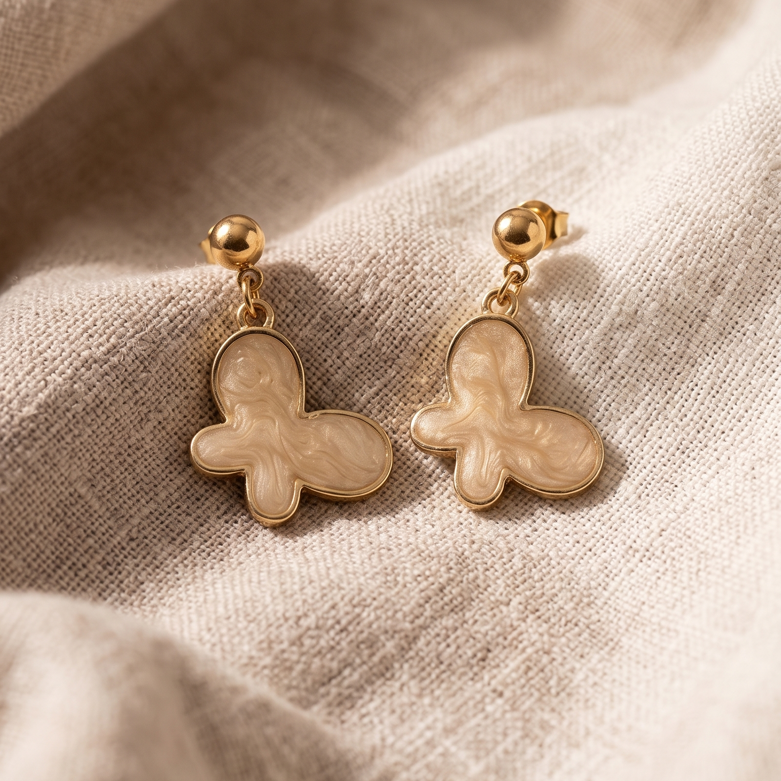 Pair of gold butterfly earrings on a beige fabric background