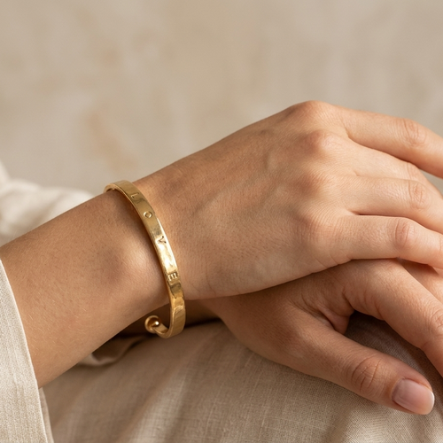 Close-up of a hand wearing a gold bracelet on a neutral background