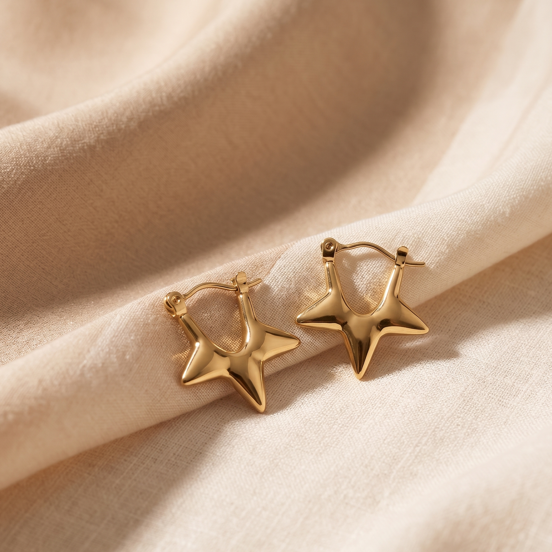 Gold star-shaped earrings on a beige fabric background