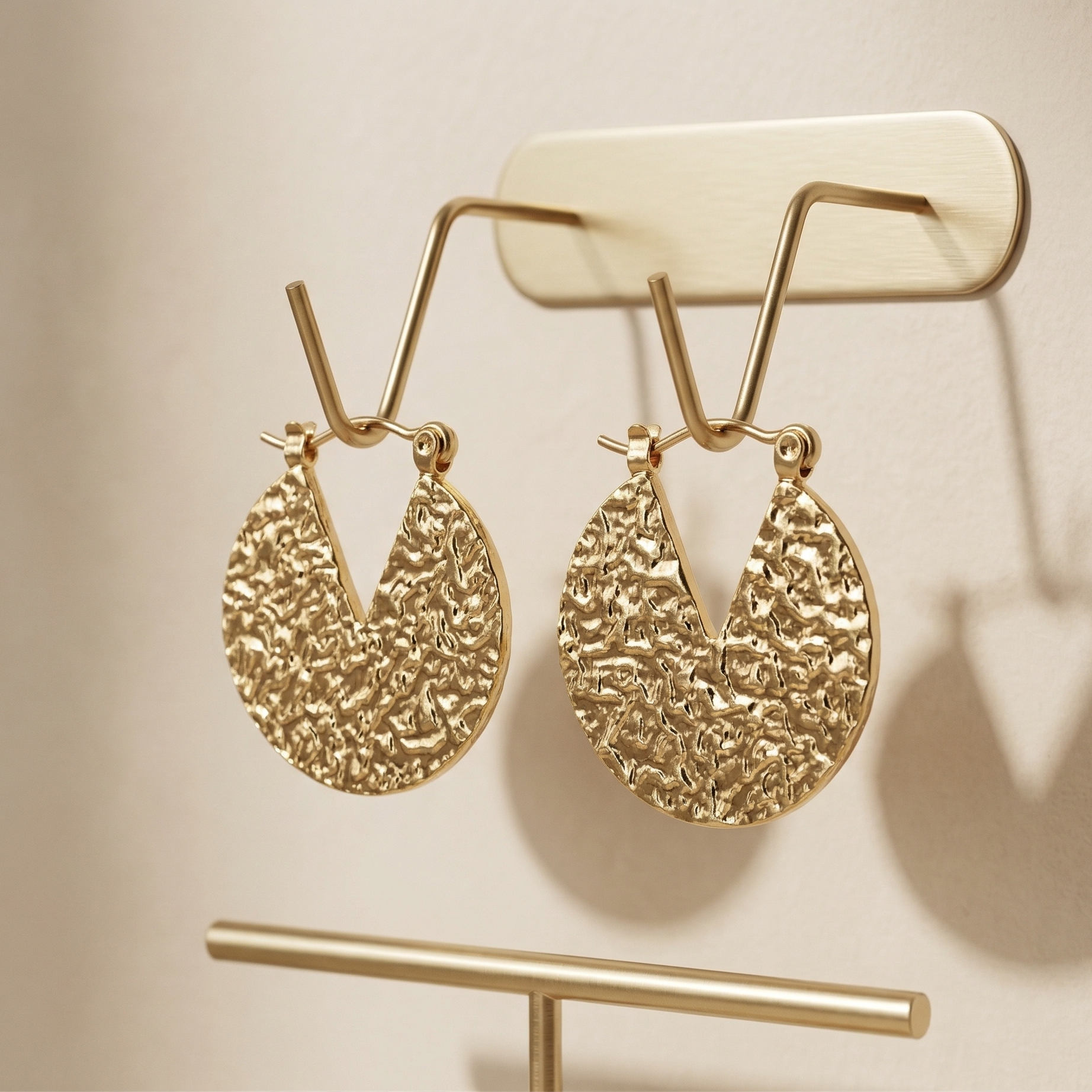 Gold textured earrings on a gold stand against a beige background