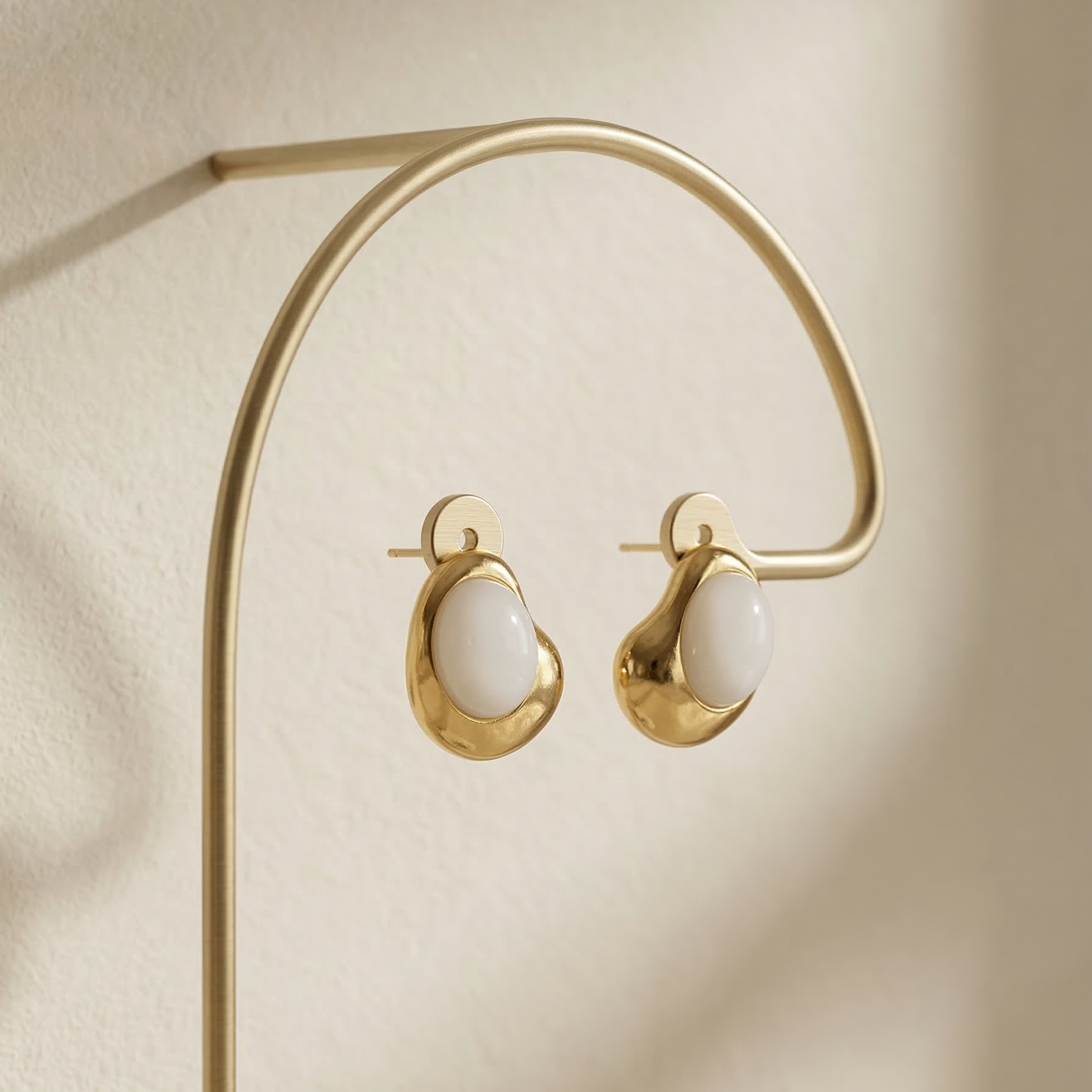 Gold hoop earrings on a gold stand against a beige background