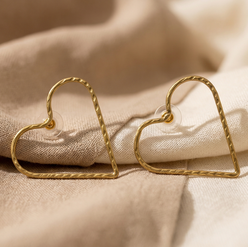 Gold heart-shaped earrings on a beige fabric background