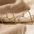 Gold heart-shaped earrings on a beige fabric background