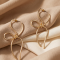 Gold bow-shaped earrings on a beige fabric background