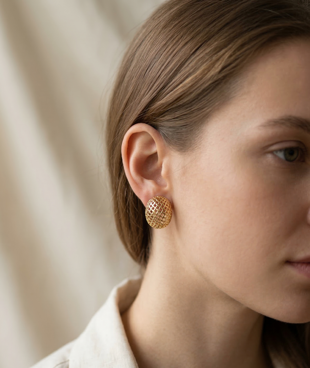 Close-up of a person wearing gold earrings with a neutral background