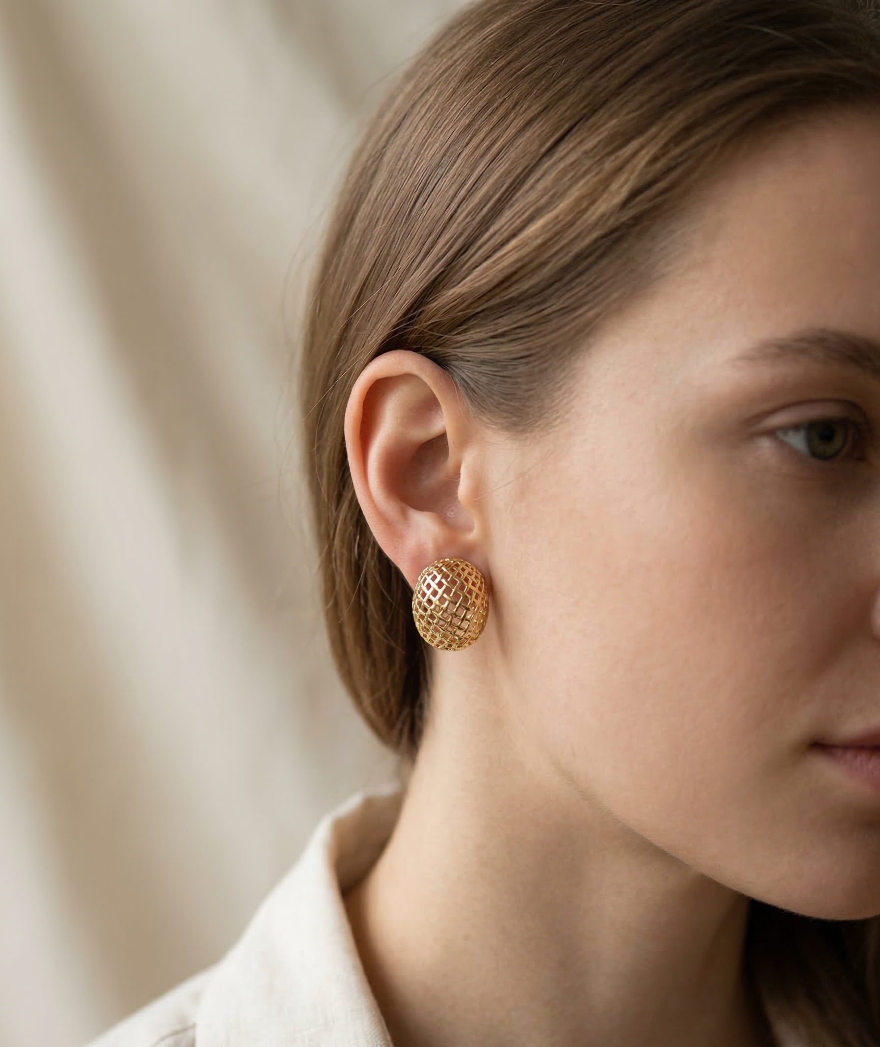 Close-up of a person wearing gold earrings with a neutral background