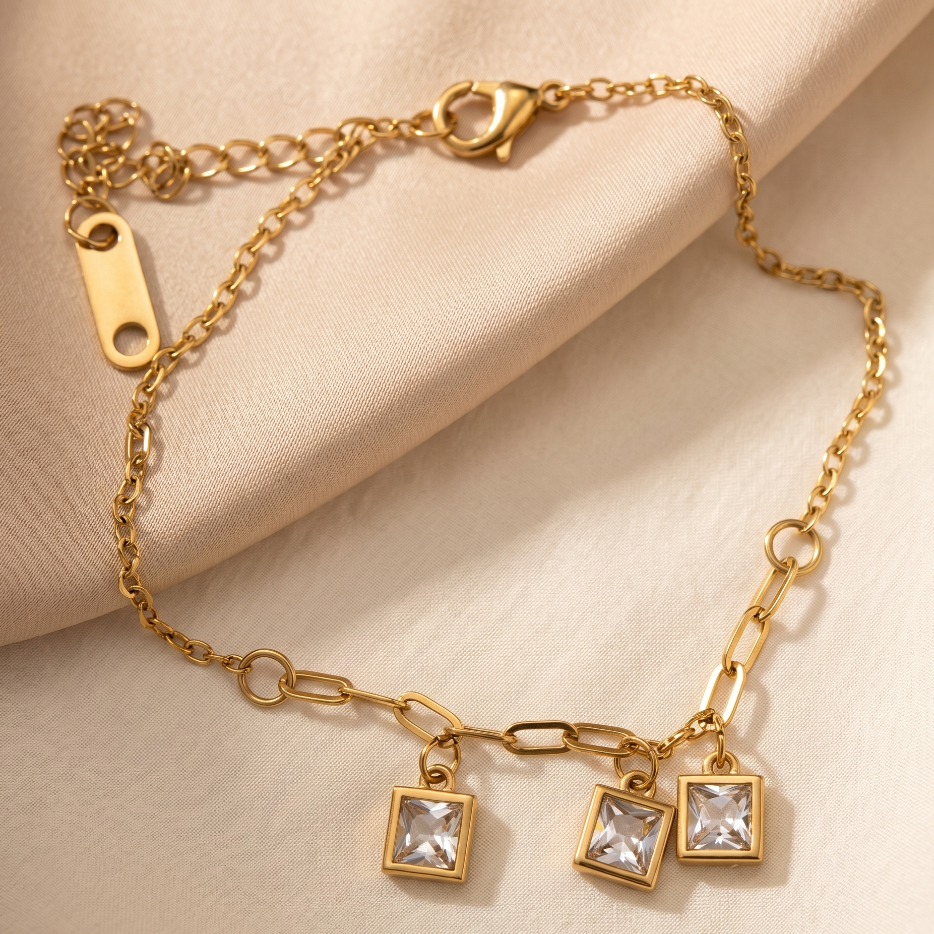 Gold bracelet with square charm on a beige fabric background