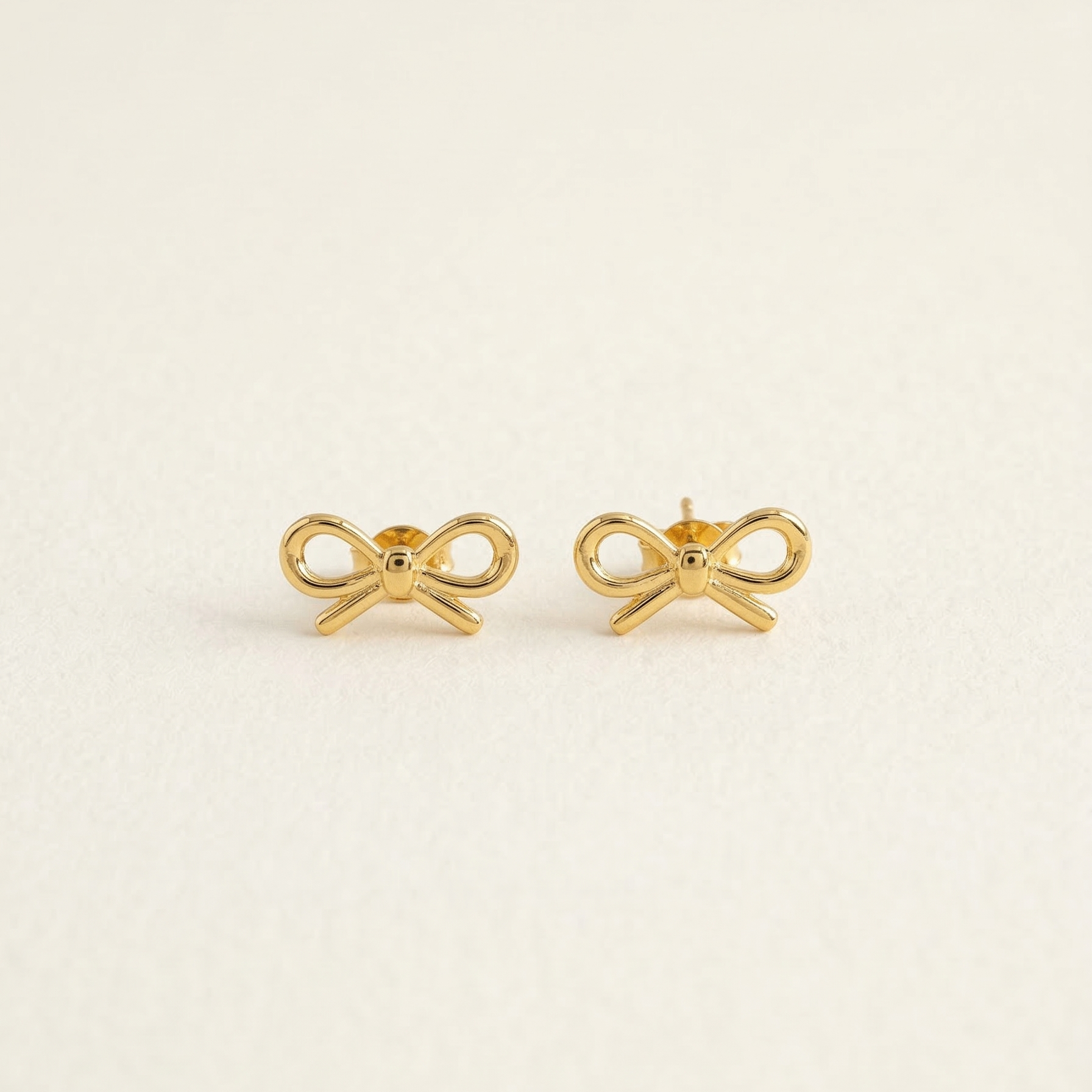 Gold bow-shaped earrings on a light beige background