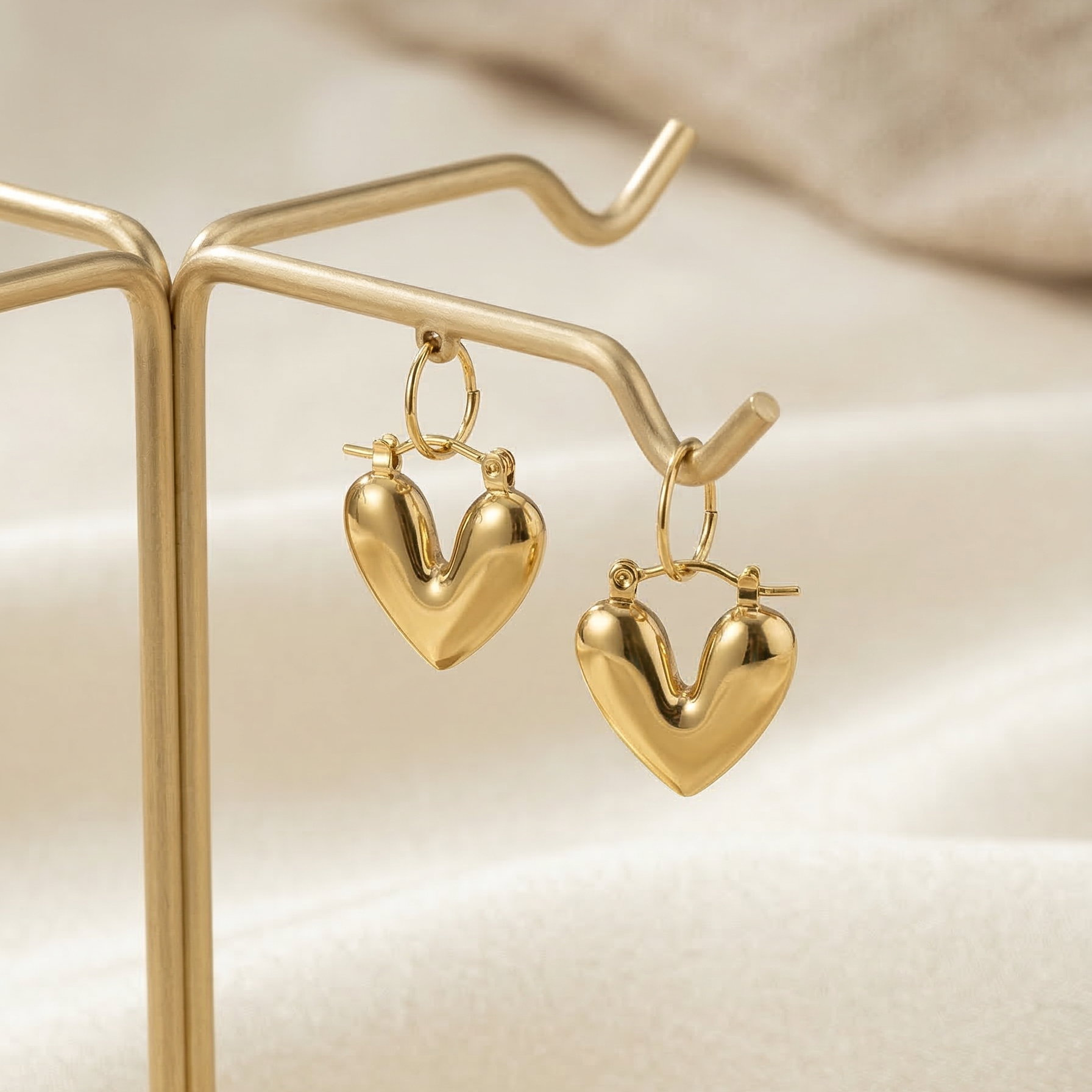 Gold heart-shaped earrings on a gold stand with a soft beige background