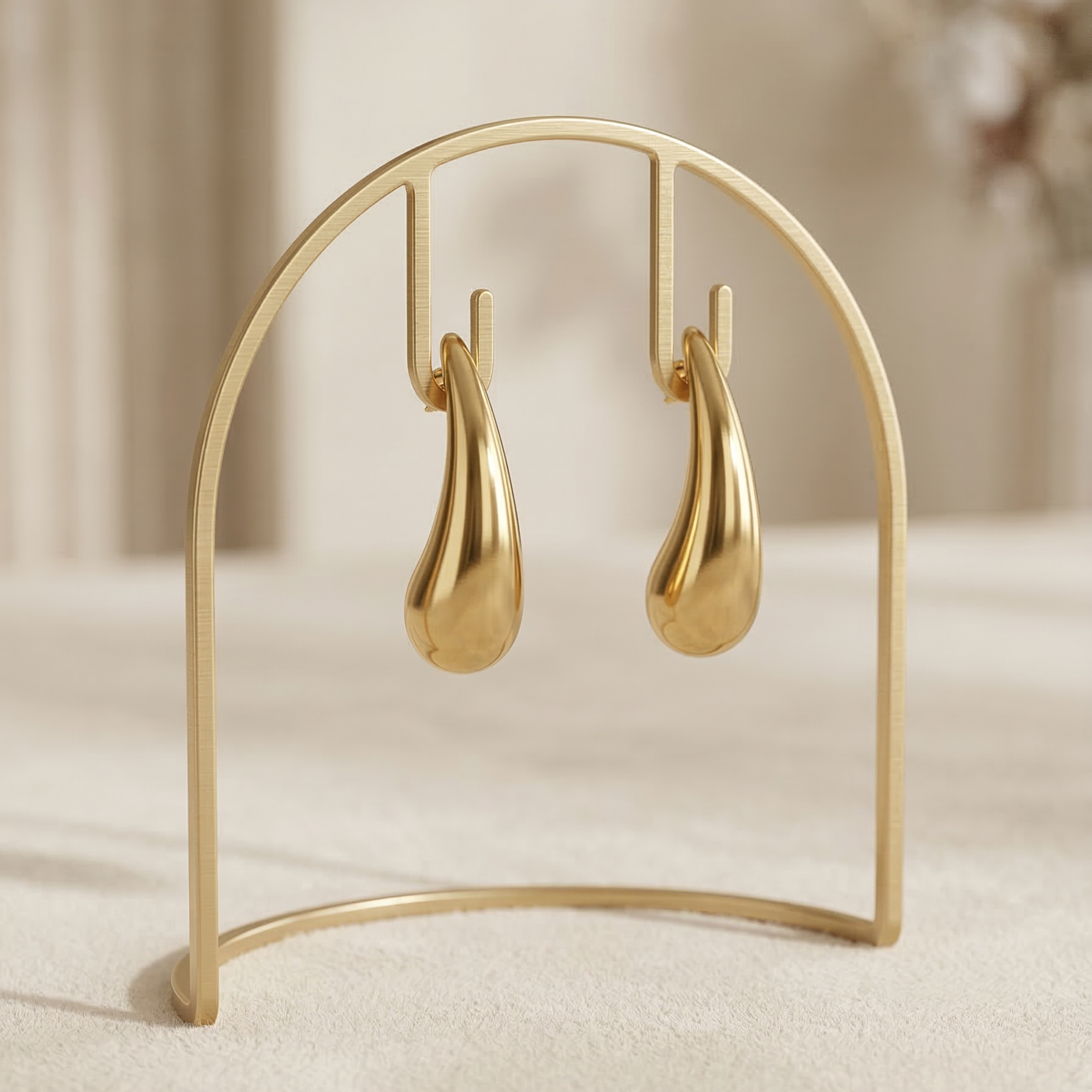 Gold teardrop earrings on a matching gold stand against a neutral background