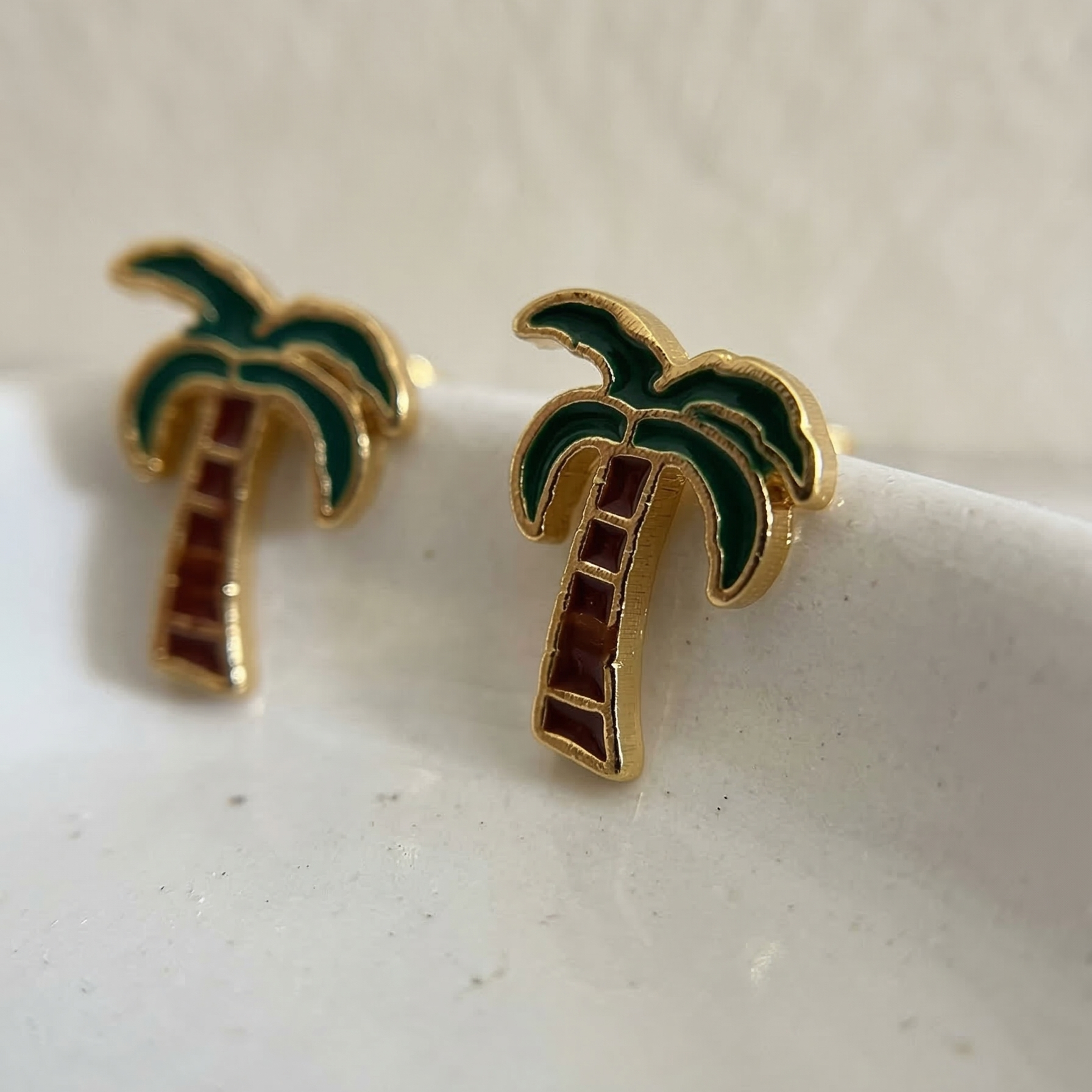 Palm tree earrings on a light beige surface