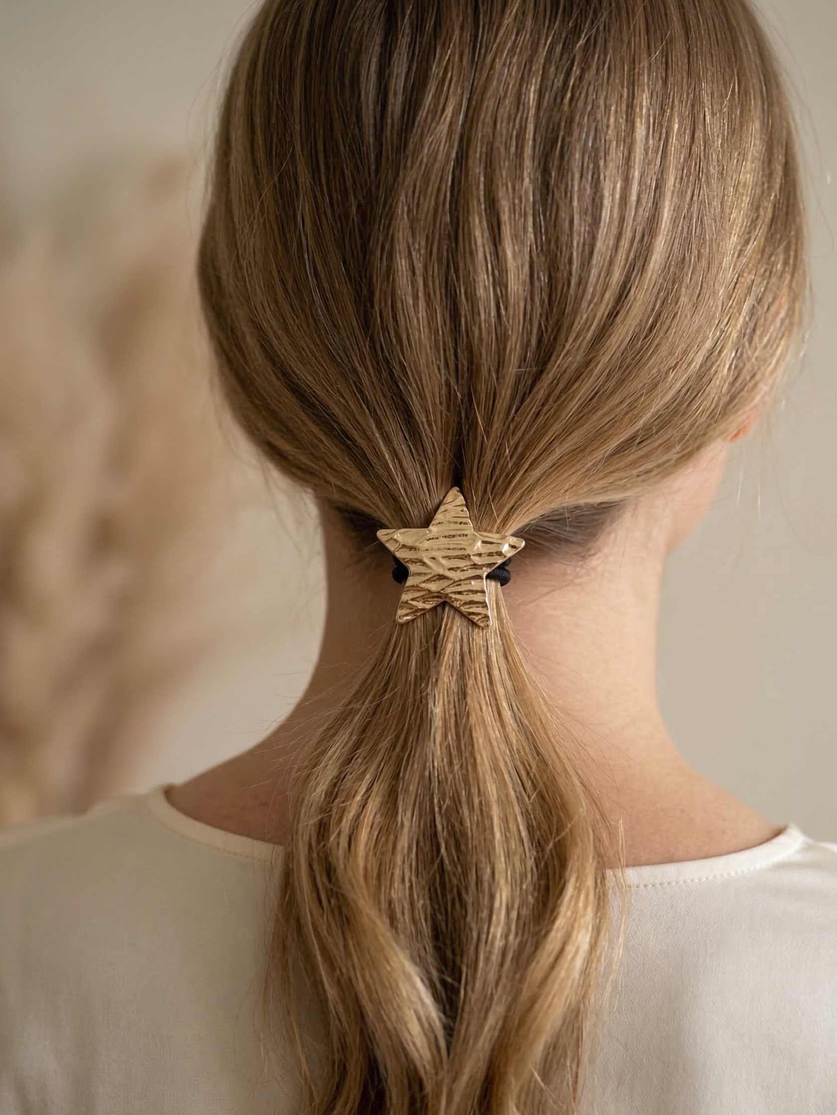 Person with blonde hair tied in a ponytail with a decorative hair tie against a neutral background