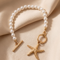Pearl bracelet with gold starfish charm on beige fabric