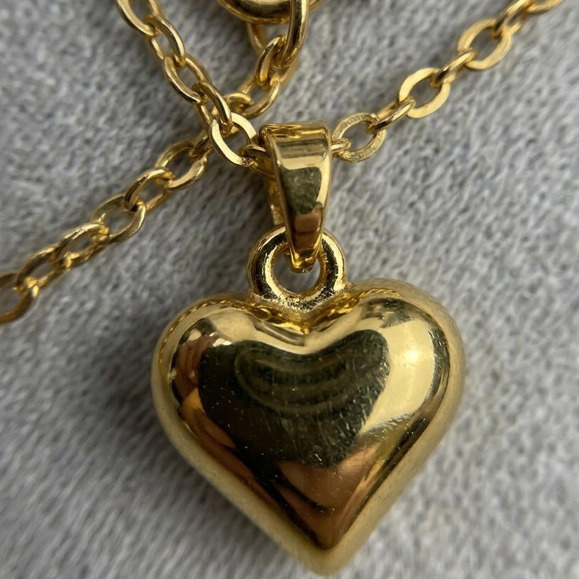 Gold heart-shaped pendant on a gold chain against a gray background