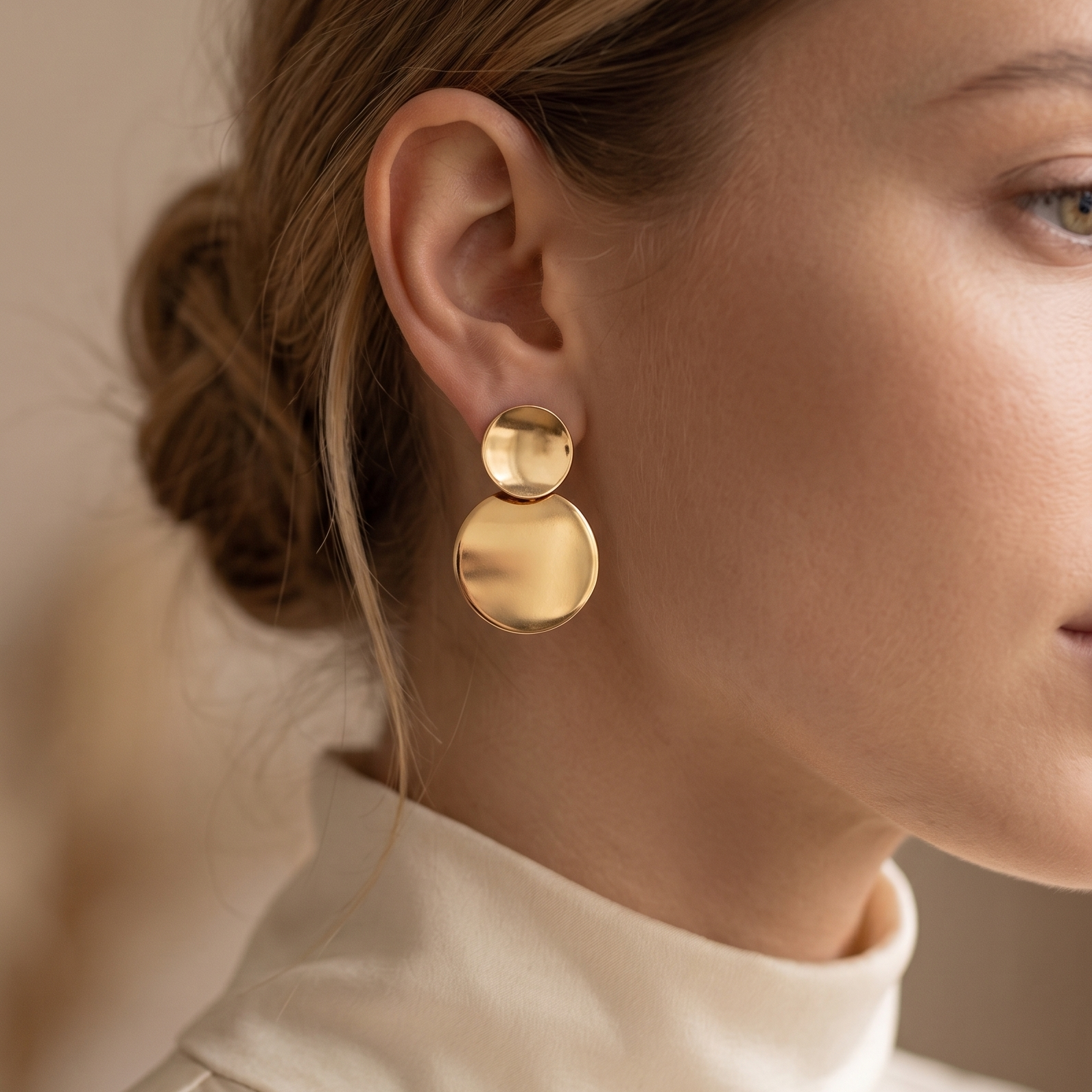 Close-up of a woman wearing gold earrings with a neutral background