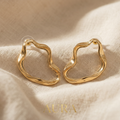 Gold hoop earrings on a beige fabric background with 'Aura' branding.