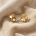 Gold earrings with pearl centers on beige fabric