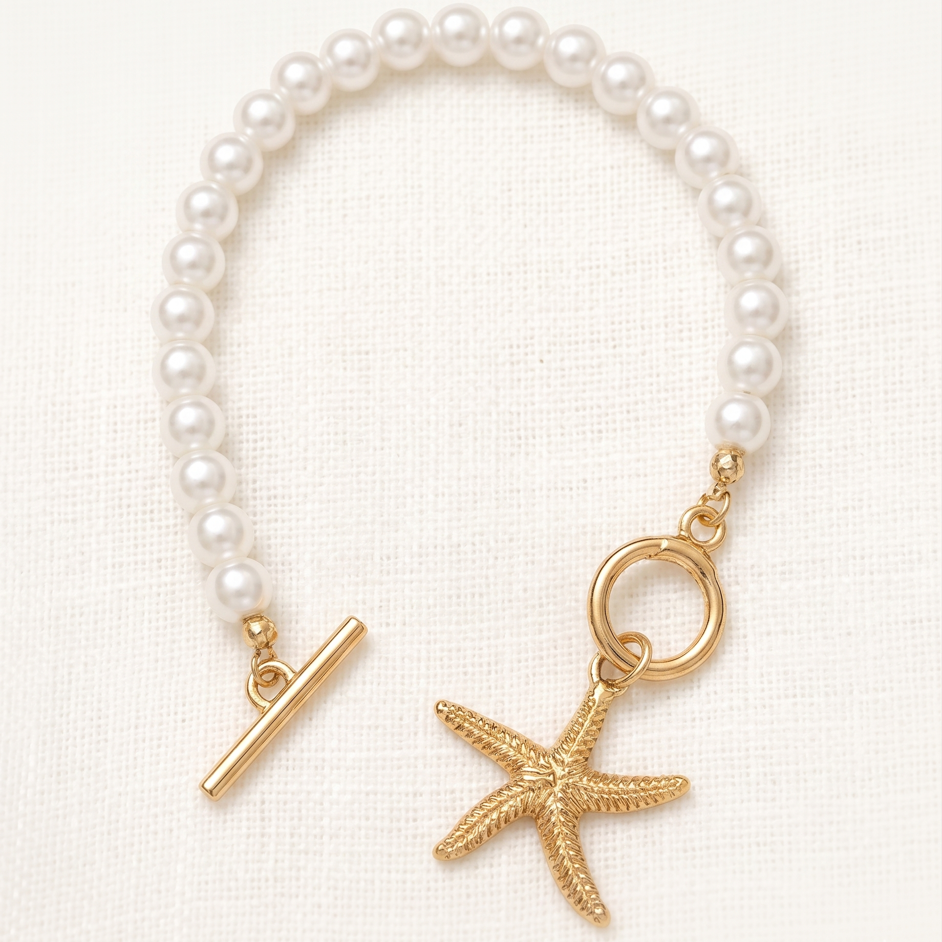 Pearl bracelet with gold clasp and starfish charm on a white background