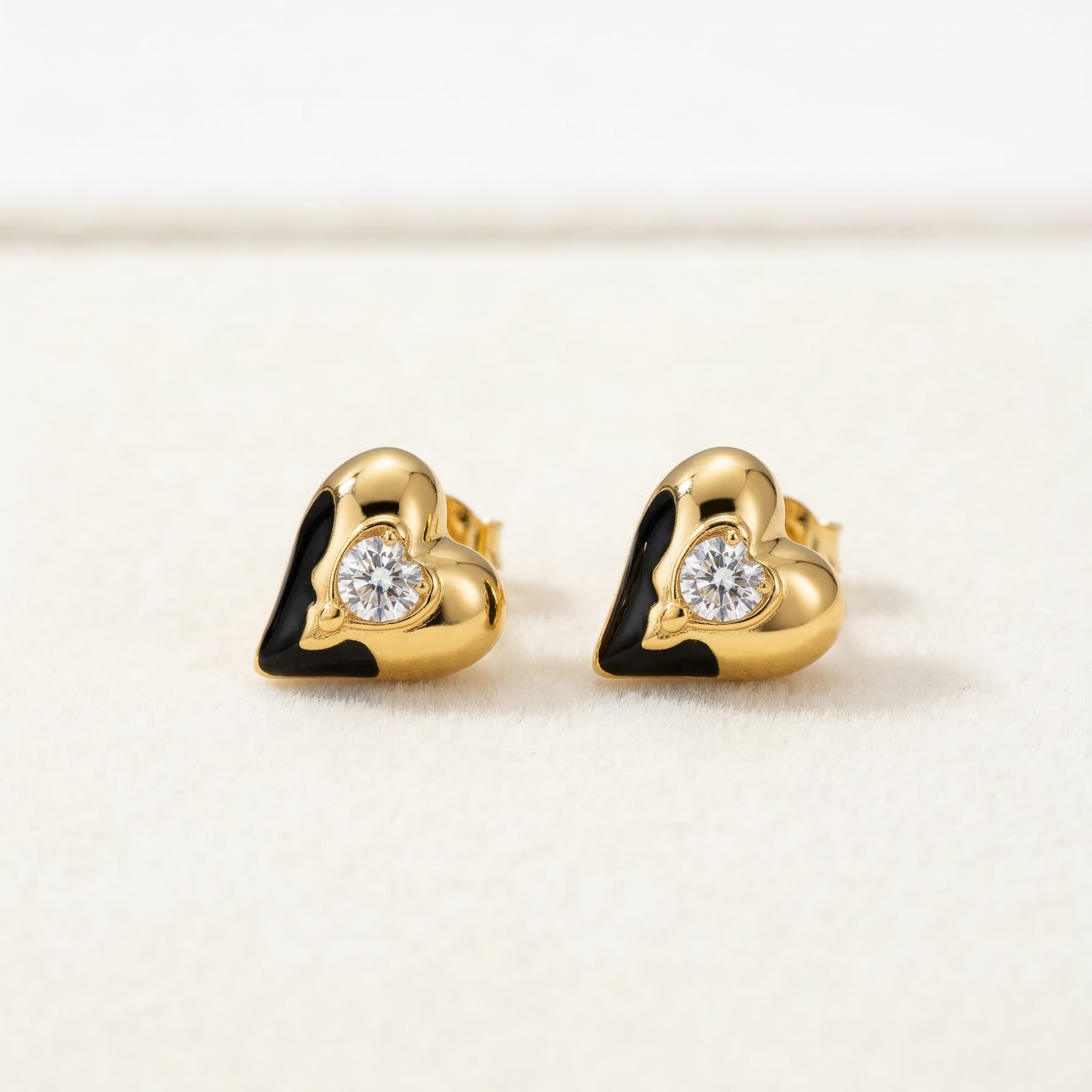Gold heart-shaped earrings with clear gemstones on a light beige background