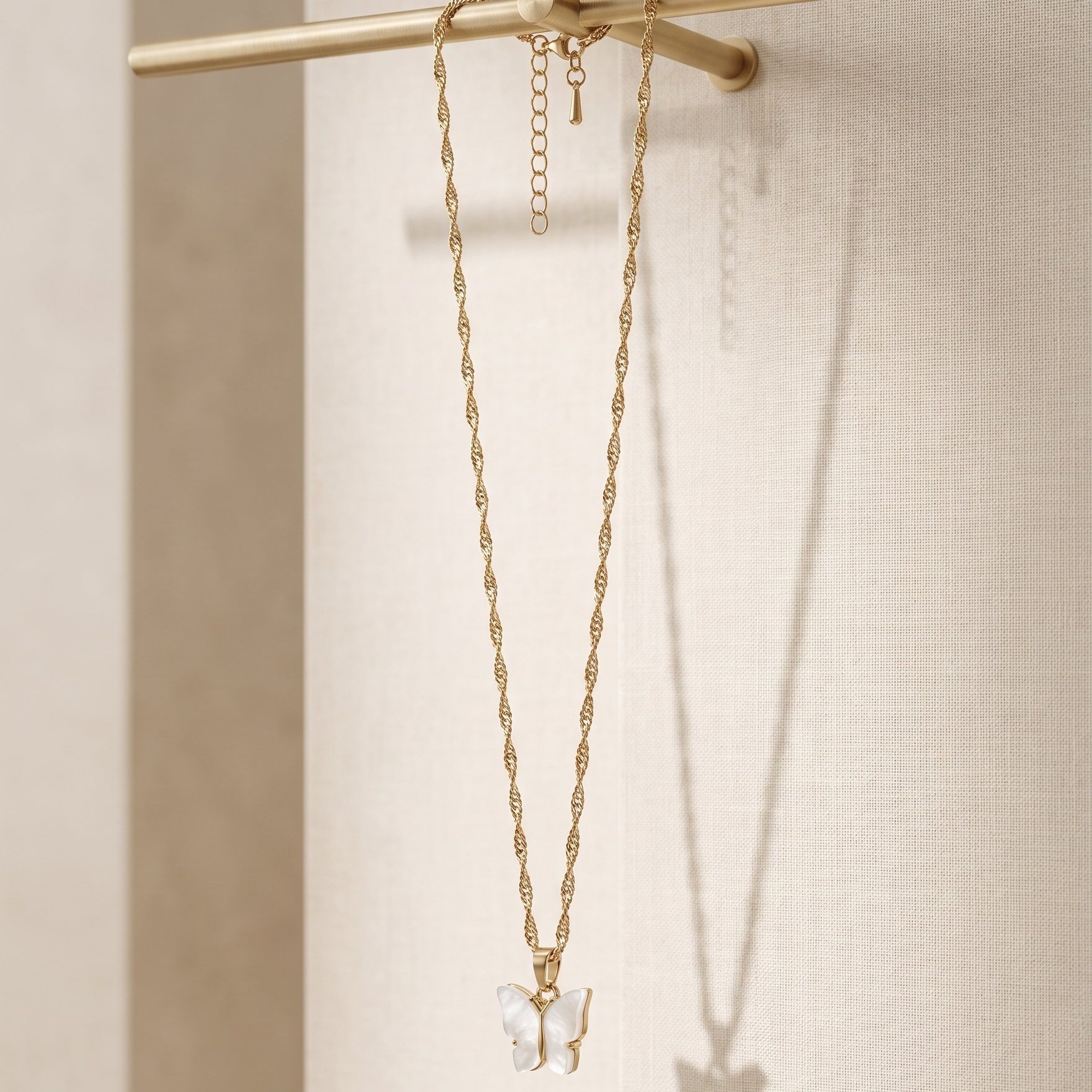 Gold necklace with a butterfly pendant on a beige background