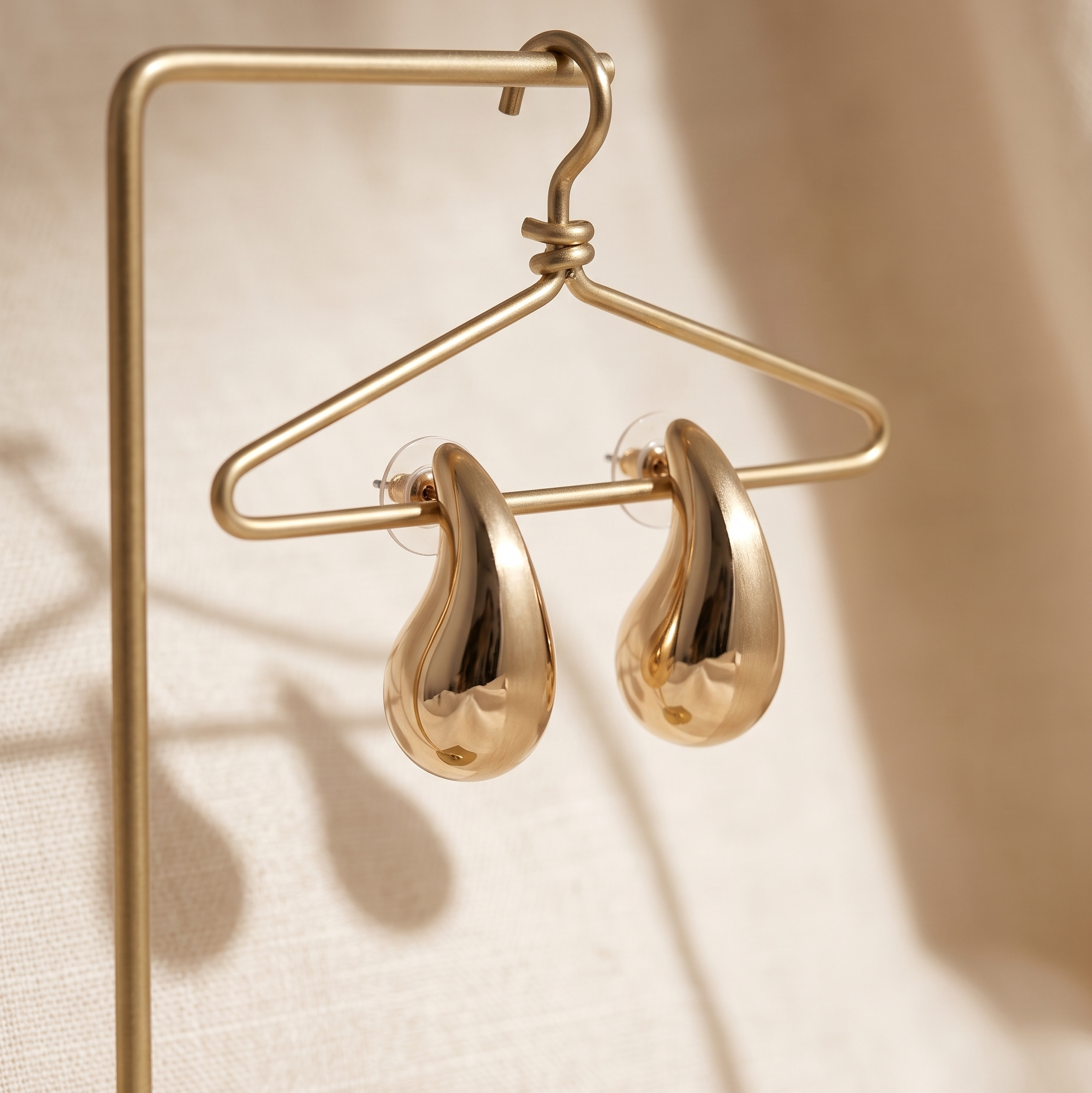 Gold earrings on a matching gold stand against a beige background