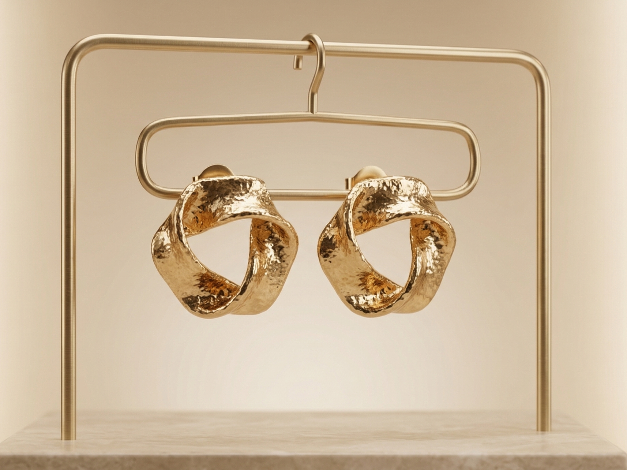 Gold hoop earrings on a gold stand against a beige background