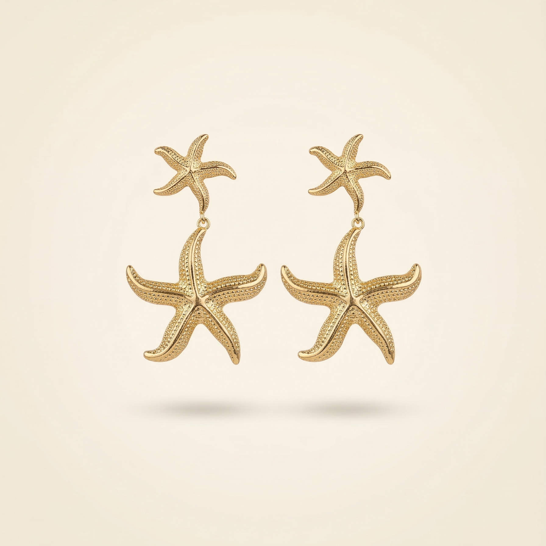 Gold starfish earrings on a beige background